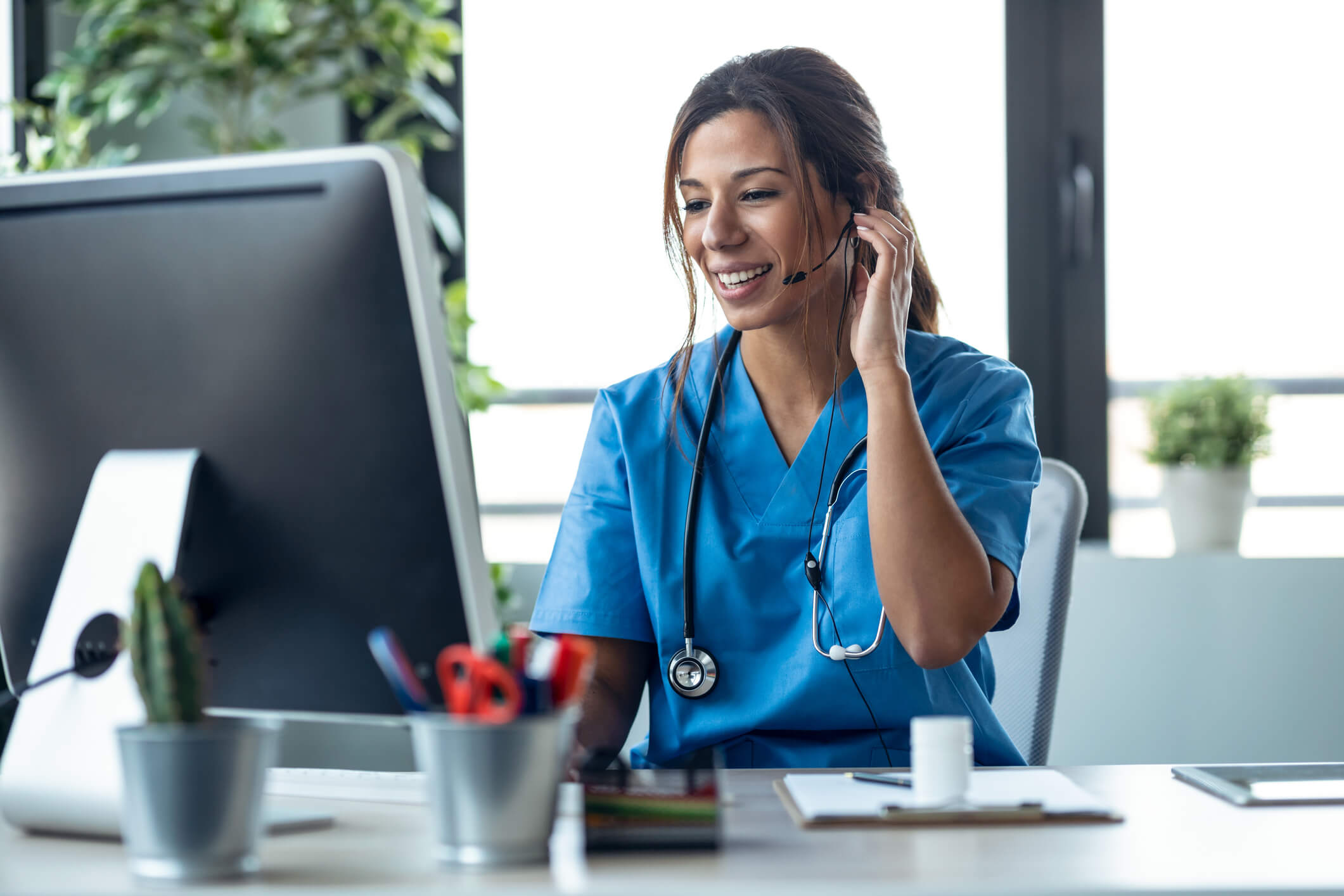 A nurse speaking with someone through a headset and viewing a computer